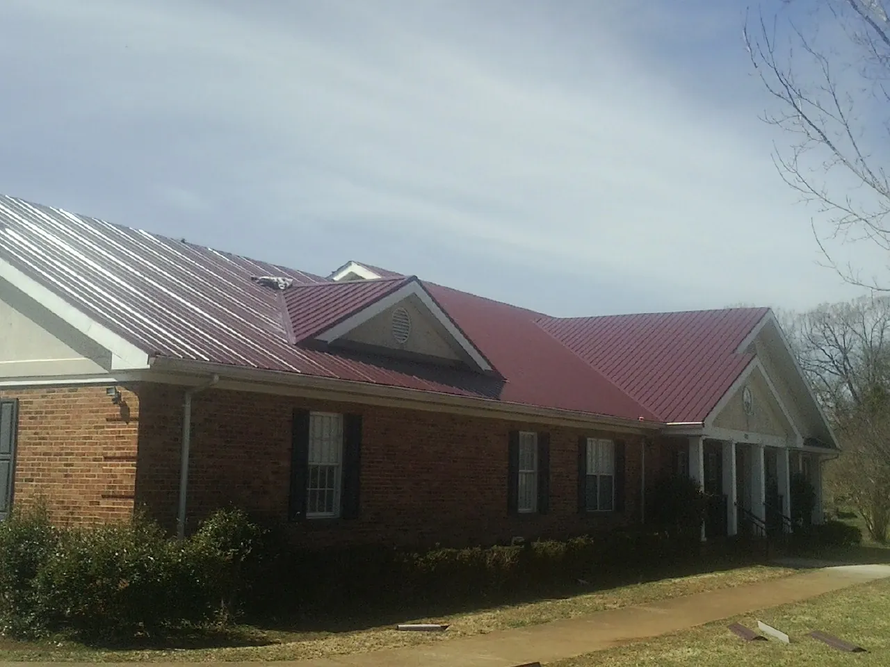 Red metal roof with gabled entries on a long brick building, from a Hail Damage Roof Repair job in Canyonville