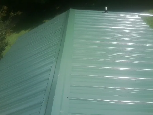 New green metal panels meeting at the ridge of a roof — Flat Roof Repair work by our crew in Canyonville