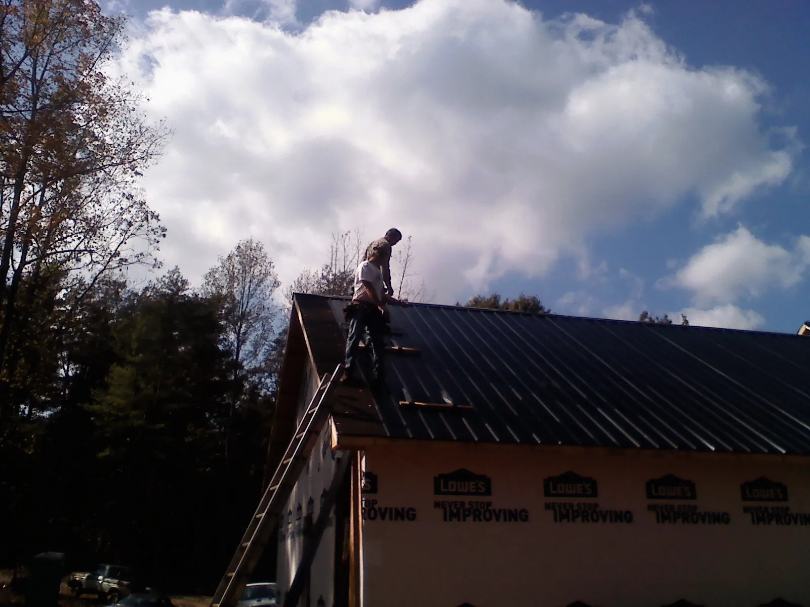 Roofer fastening dark metal panels high against a cloudy sky in Canyonville