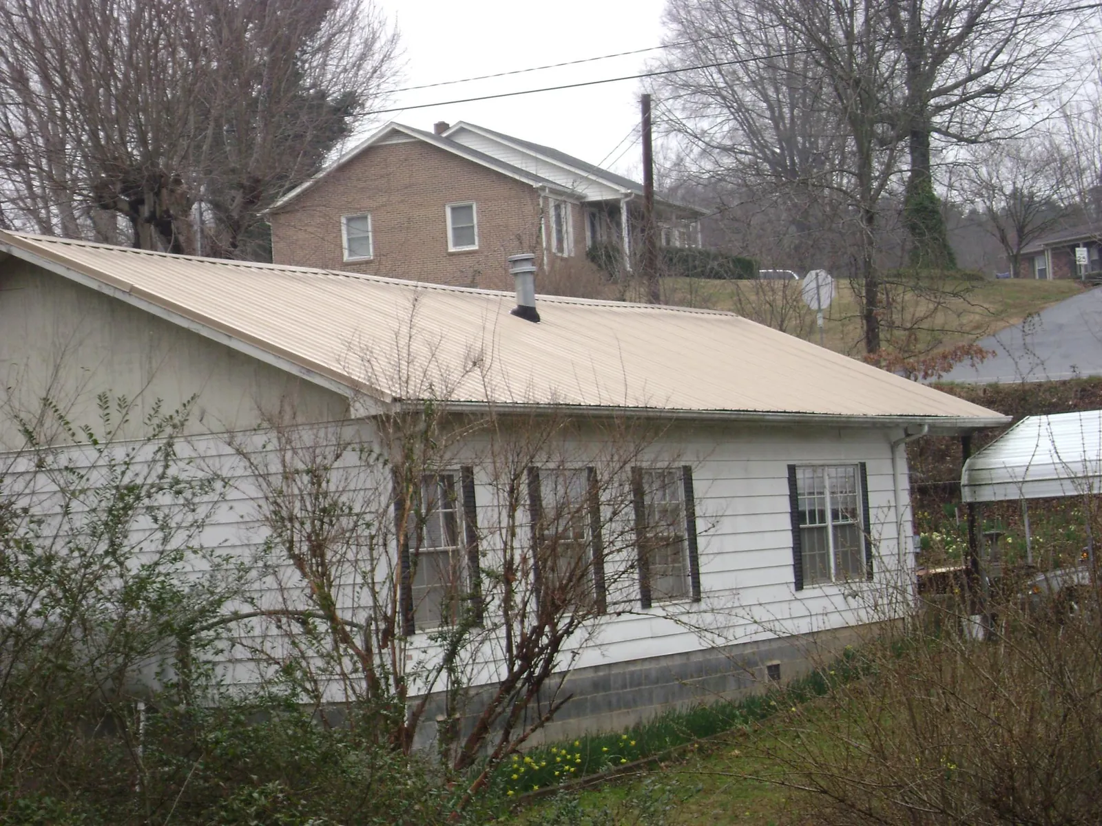 Tan metal roof on a white sided house set into a hillside — Commercial Roofing by Roofing Brothers in Canyonville